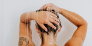 Person washing their hair under a running shower in a modern bathroom